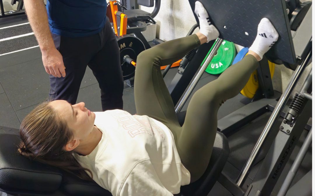A physiotherapist supervising a client on a leg press during rehabilitation.