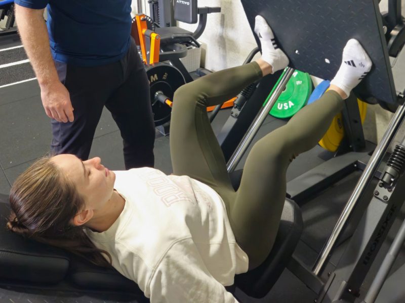 A physiotherapist supervising a client on a leg press during rehabilitation.