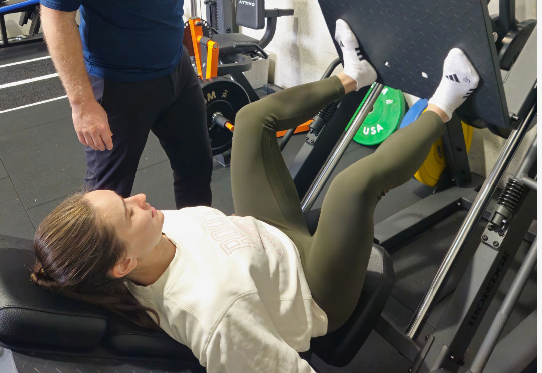 A physiotherapist supervising a client on a leg press during rehabilitation.