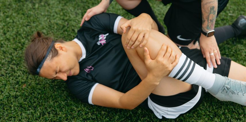 Female footballer lying on the pitch clutching her knee after a suspected ACL injury