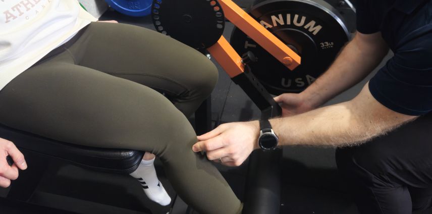 Physiotherapist adjusting a patient's leg during a seated leg-press exercise