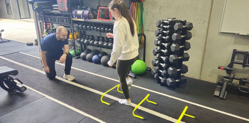Physiotherapist coaching an athlete through an agility hurdle drill in the gym