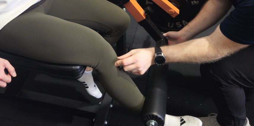Physiotherapist adjusting a patient's leg during a seated leg-press exercise