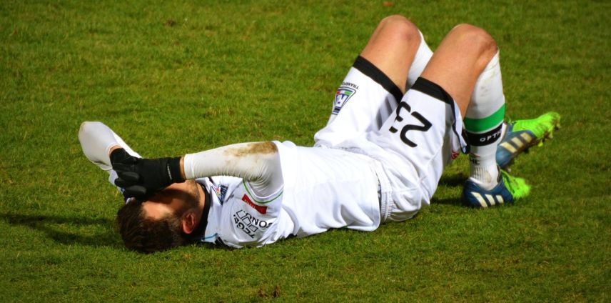 Footballer lying on the pitch holding his head after a head knock
