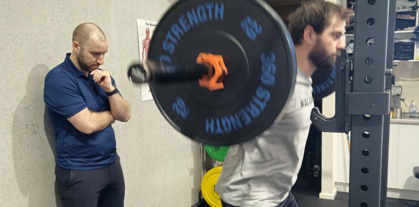 Physiotherapist observing an athlete performing a barbell squat