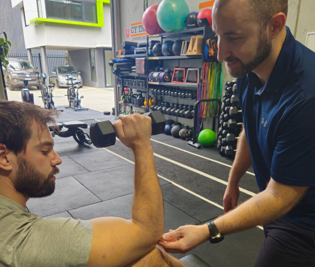 A physiotherapist guiding a client through shoulder rehabilitation exercises in the gym.