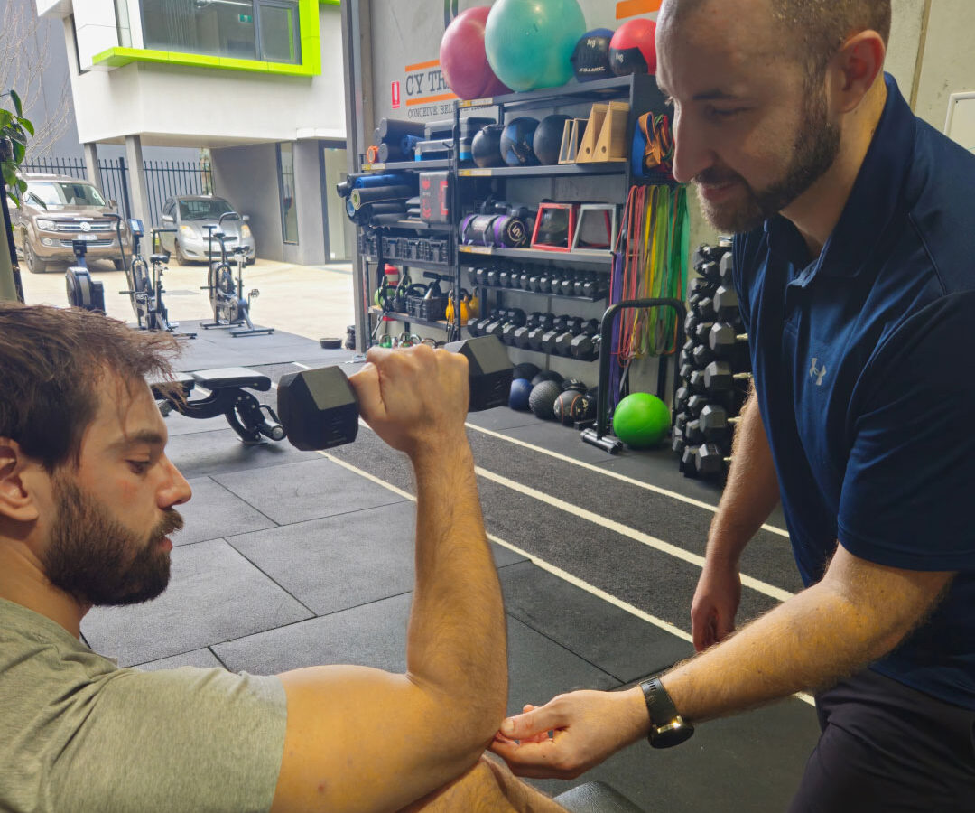 A physiotherapist guiding a client through shoulder rehabilitation exercises in the gym.