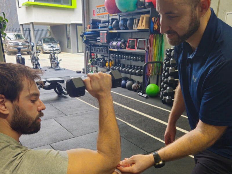 A physiotherapist guiding a client through shoulder rehabilitation exercises in the gym.