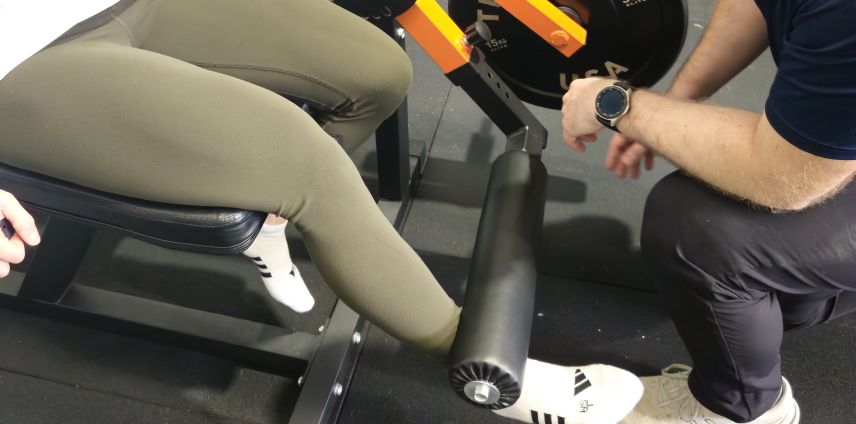 Physiotherapist adjusting a patient's leg on a leg-curl machine