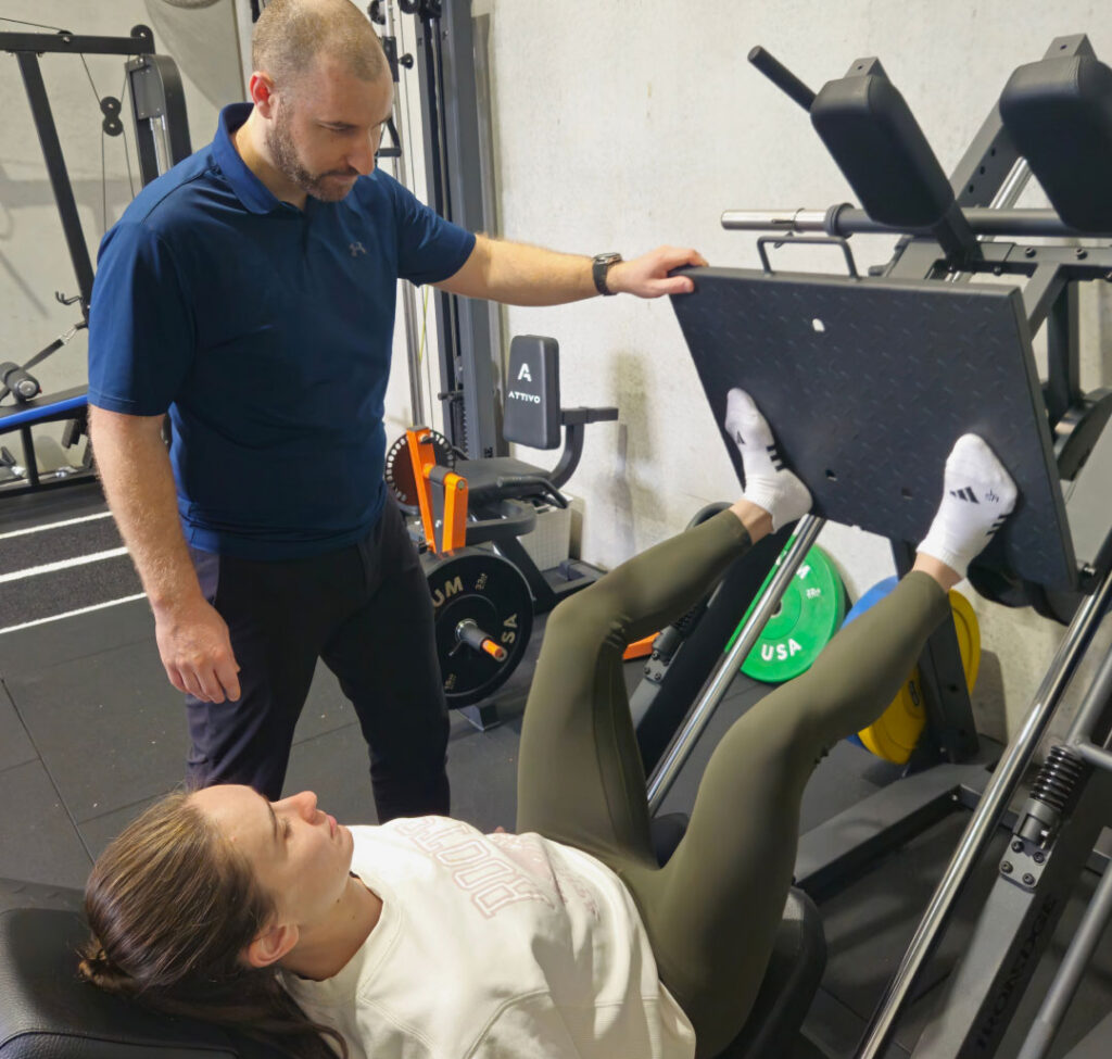 A physiotherapist supervising a client on the leg press machine during rehabilitation.