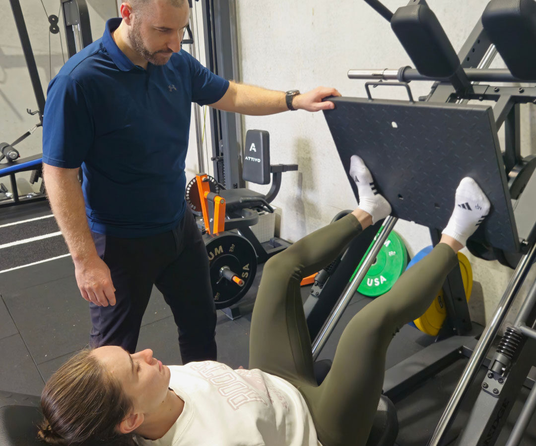 A physiotherapist supervising a client on the leg press machine during rehabilitation.
