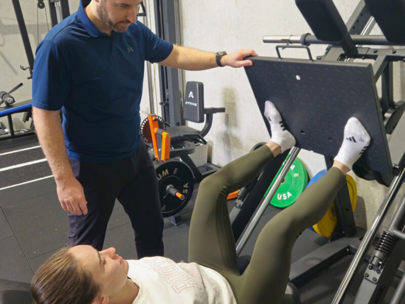 A physiotherapist supervising a client on the leg press machine during rehabilitation.