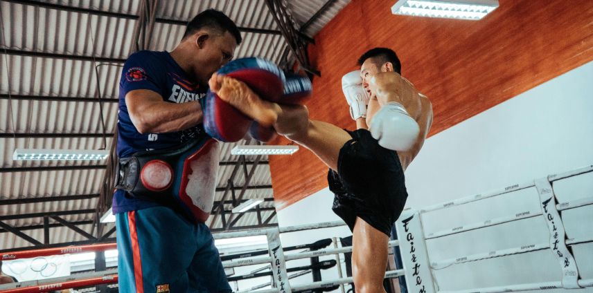 Muay Thai fighter delivering a high kick to focus mitts held by a trainer