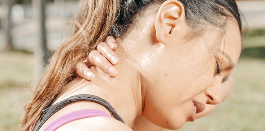 Woman outdoors holding the back of her neck in discomfort