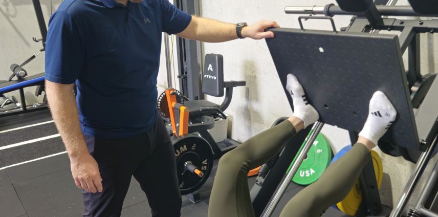 Physiotherapist standing beside a leg-press machine during a patient's rehab session