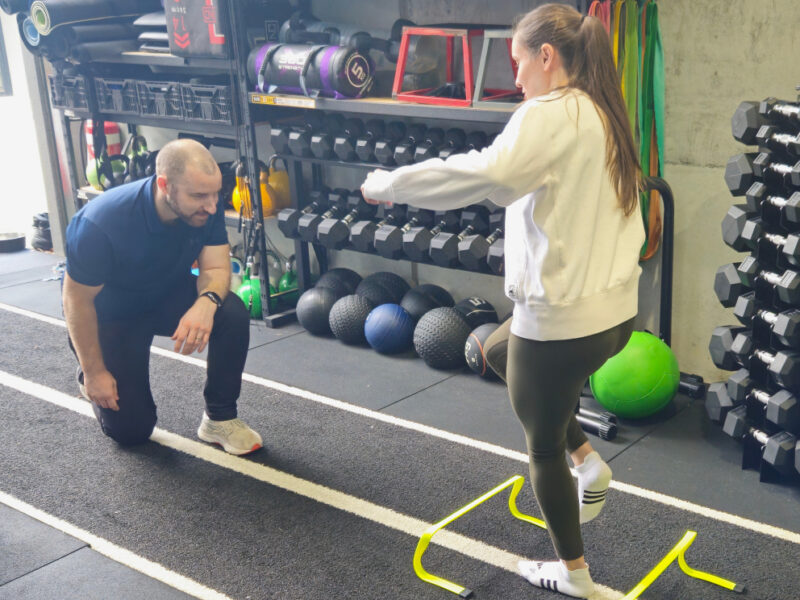 A physiotherapist guiding a client through an agility drill over hurdles in the rehabilitation gym.