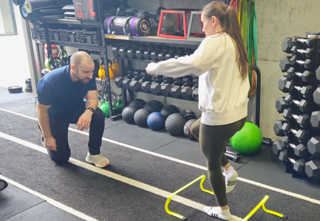 A physiotherapist guiding a client through an agility drill over hurdles in the rehabilitation gym.