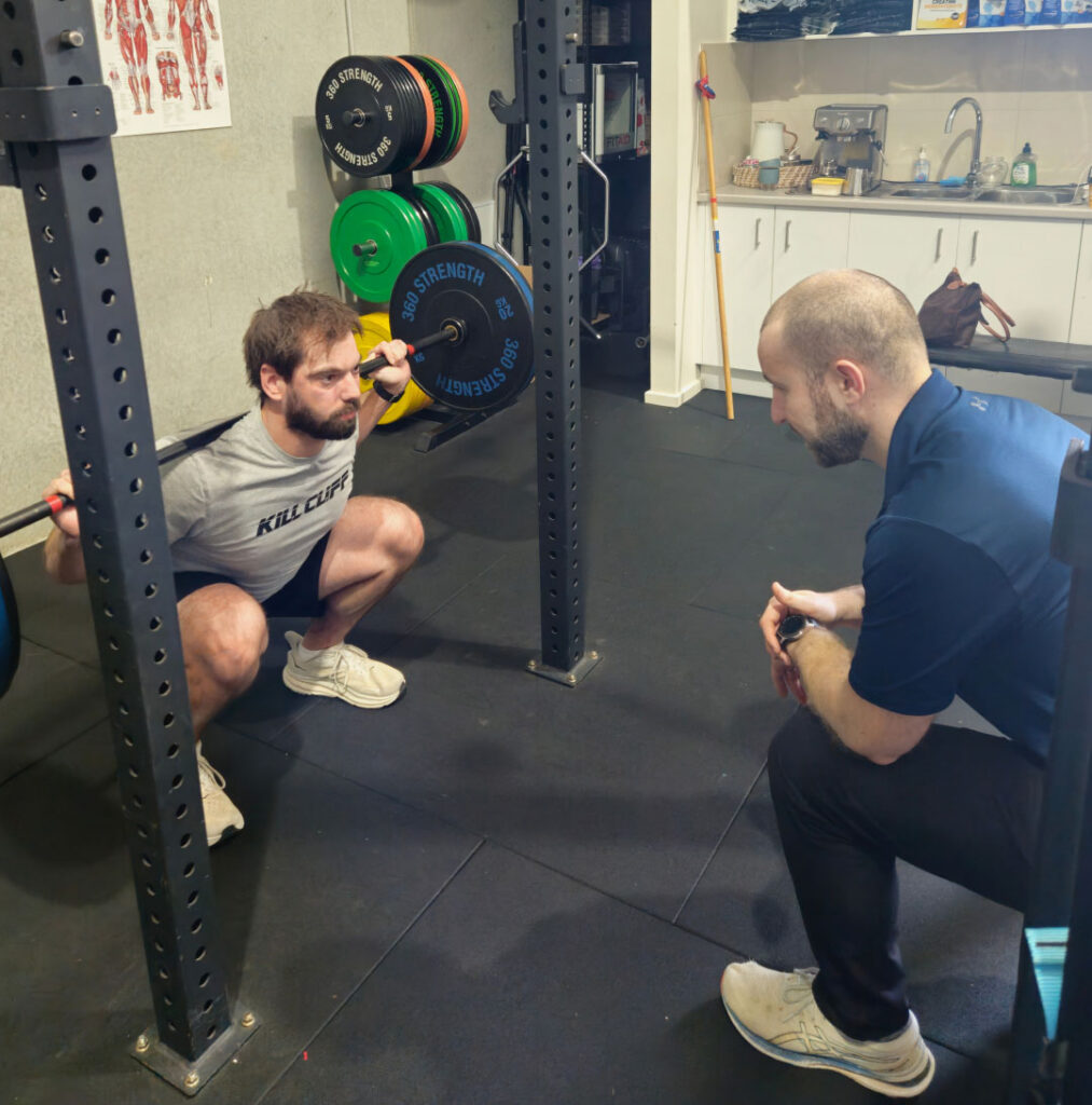 A physiotherapist guiding a client through a squat exercise in the gym.
