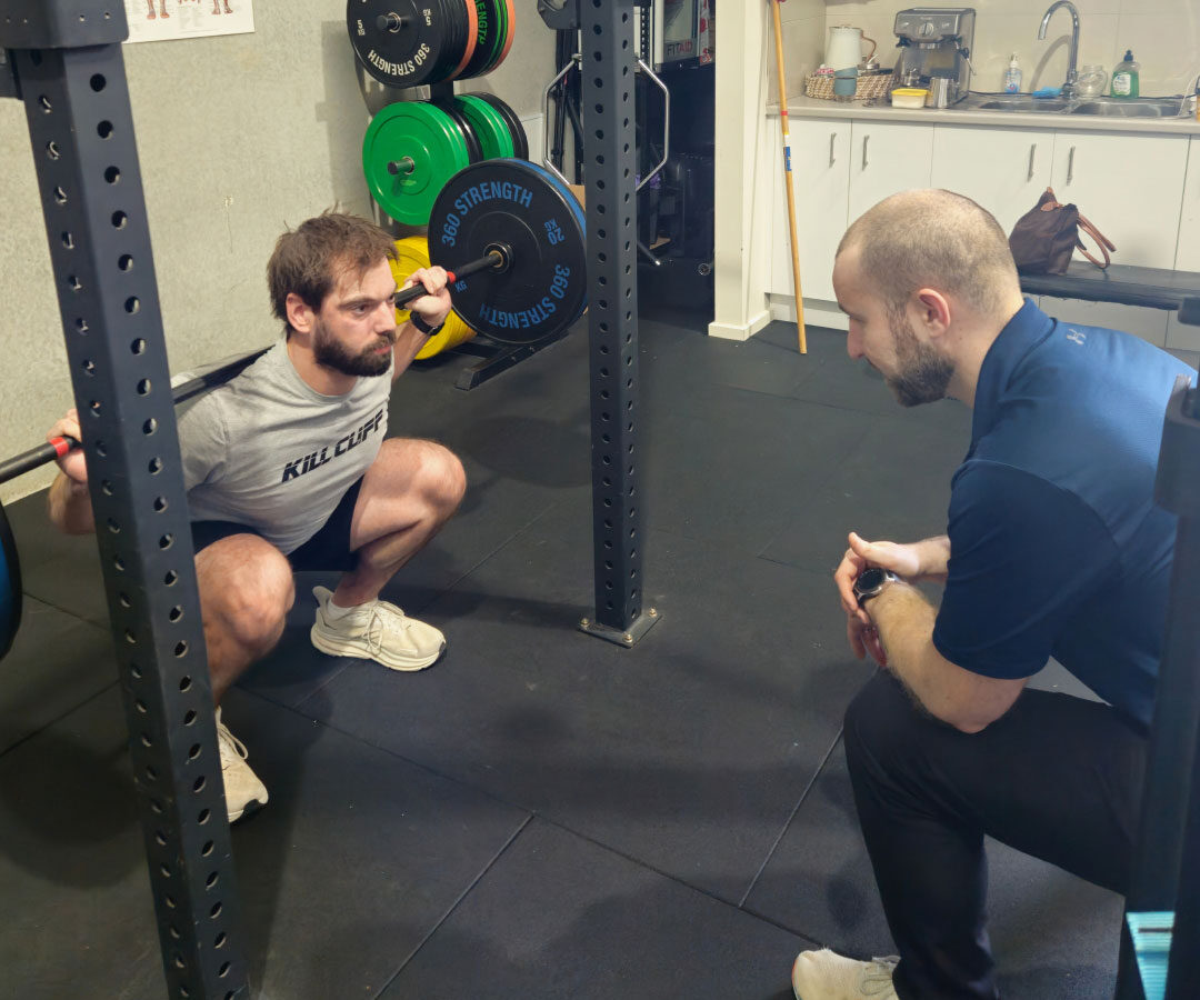 A physiotherapist guiding a client through a squat exercise in the gym.