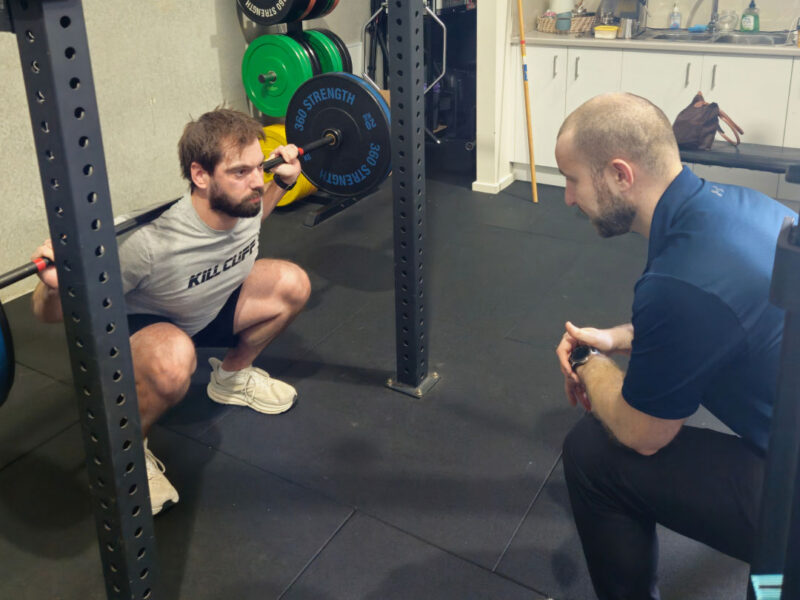 A physiotherapist guiding a client through a squat exercise in the gym.