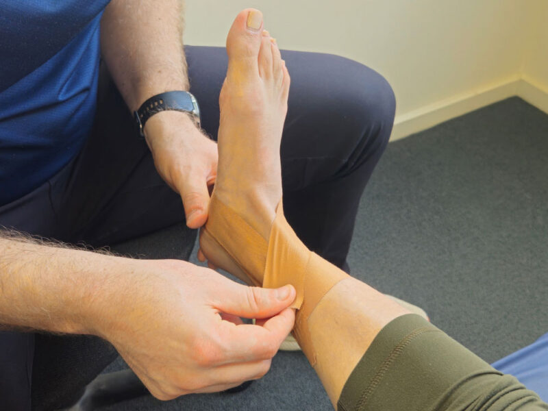 A physiotherapist taping a client's ankle in the clinic.