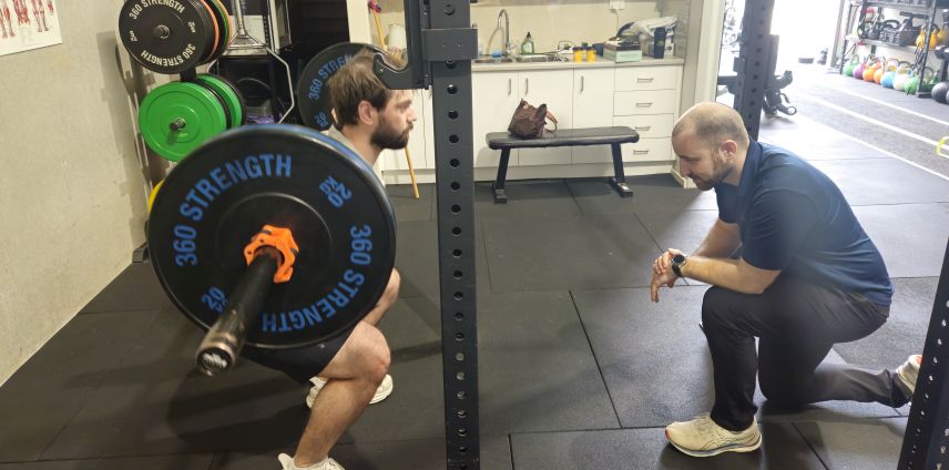 Physiotherapist timing an athlete's barbell squat during a gym session