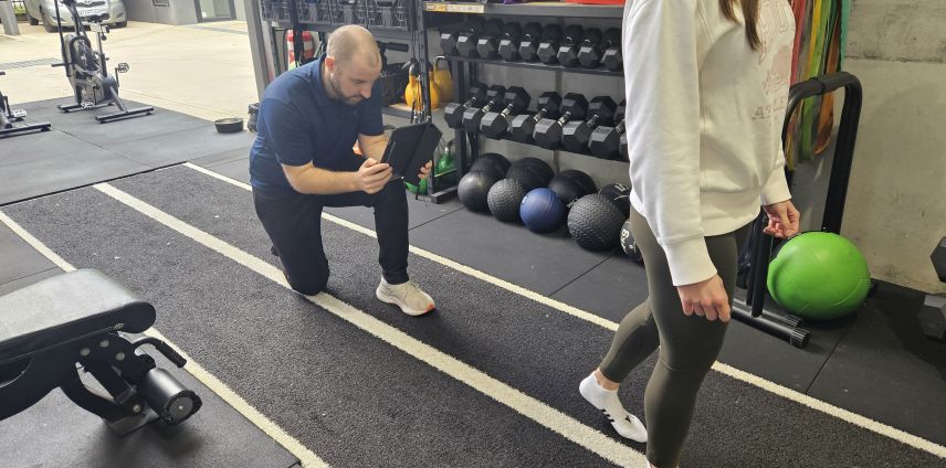 Physiotherapist reviewing data on a tablet while a runner passes by on an indoor track