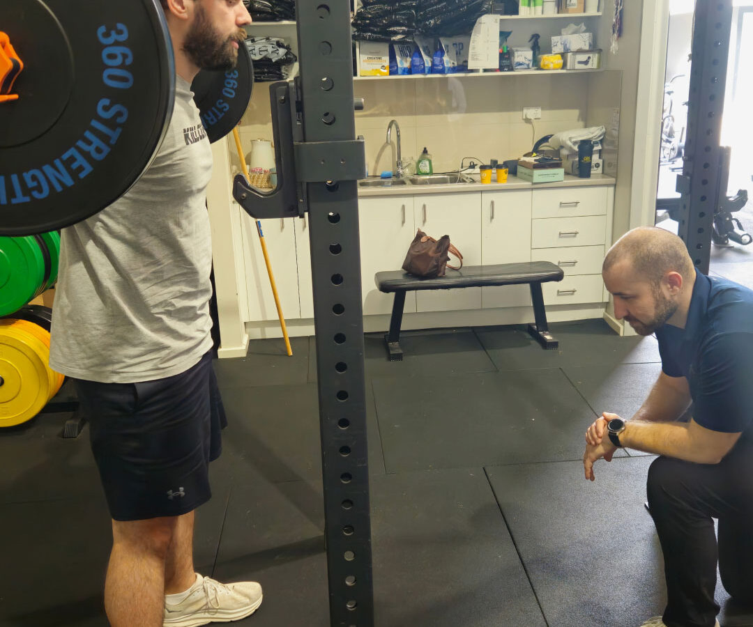 A sports physiotherapist guiding a client through gym-based rehabilitation.