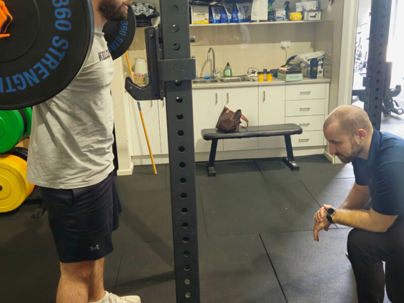 A sports physiotherapist guiding a client through gym-based rehabilitation.