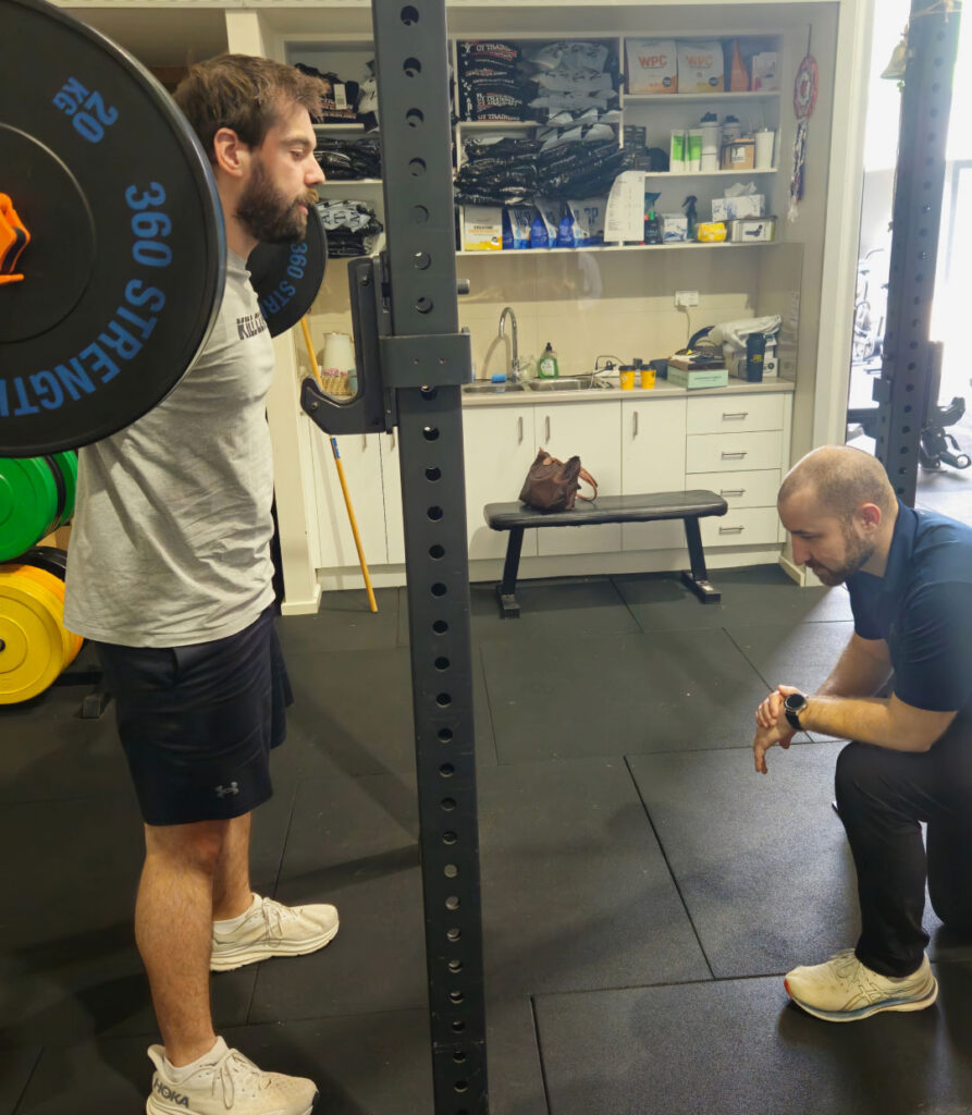 A sports physiotherapist guiding a client through gym-based rehabilitation.